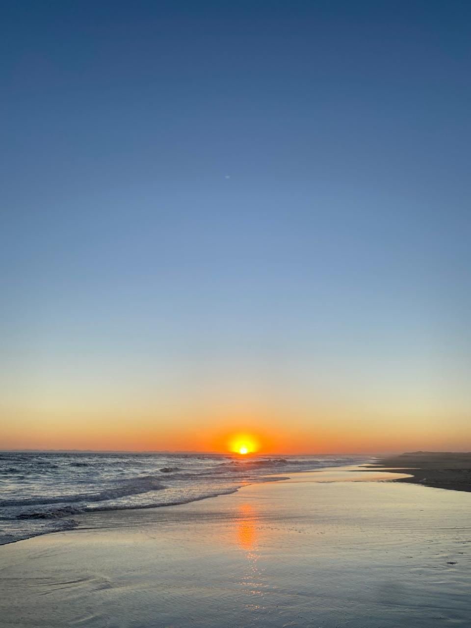 Sol poniéndose sobre la orilla, con el mar y la arena mojada