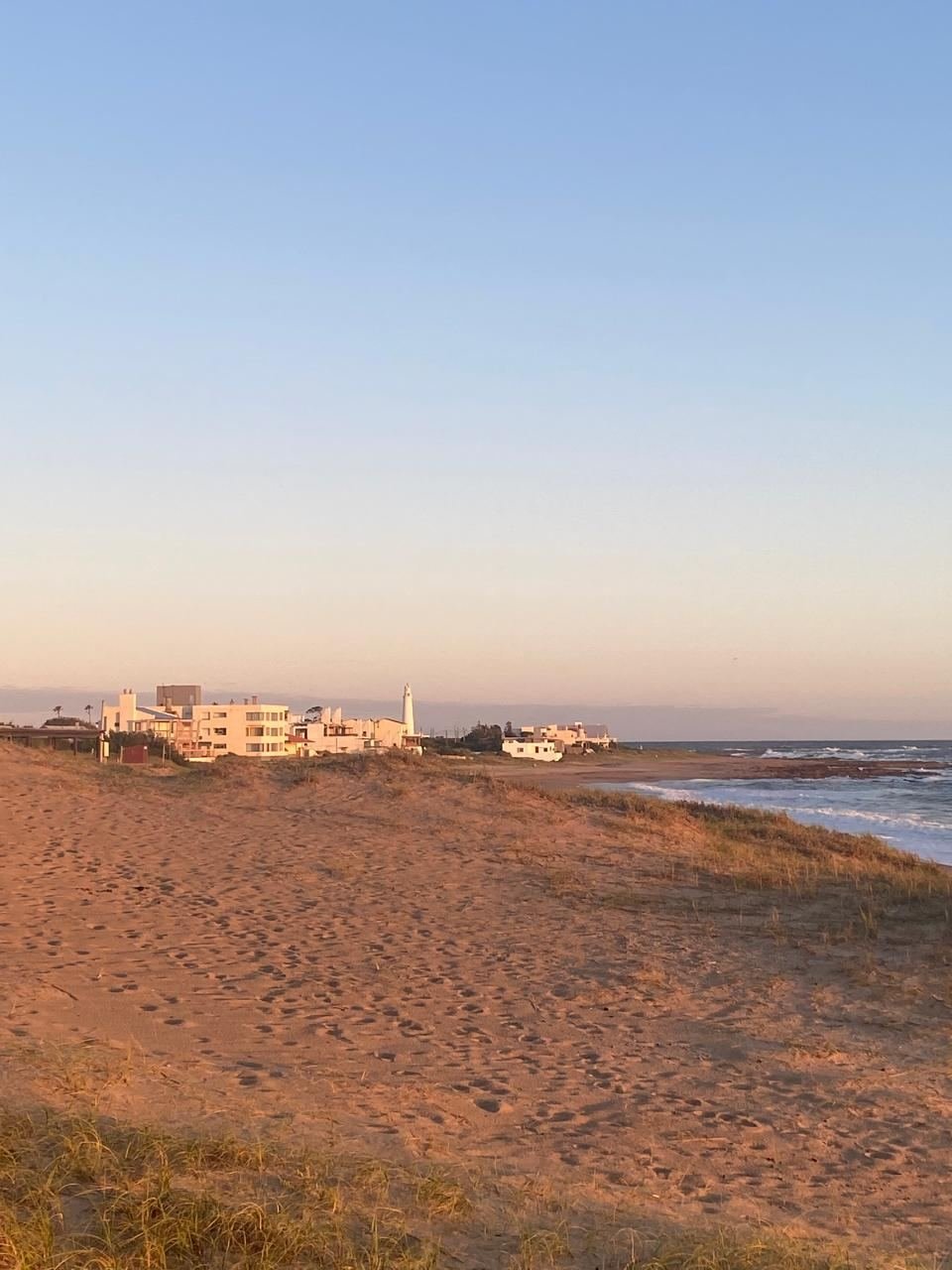 Duna con casas blancas y el faro al fondo, bajo luz rosada de la tarde