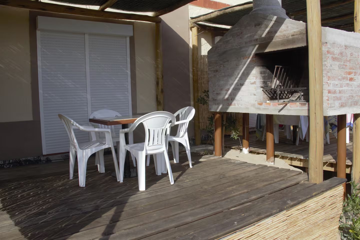 Deck de madera con mesa y sillas blancas y parrillero de ladrillo