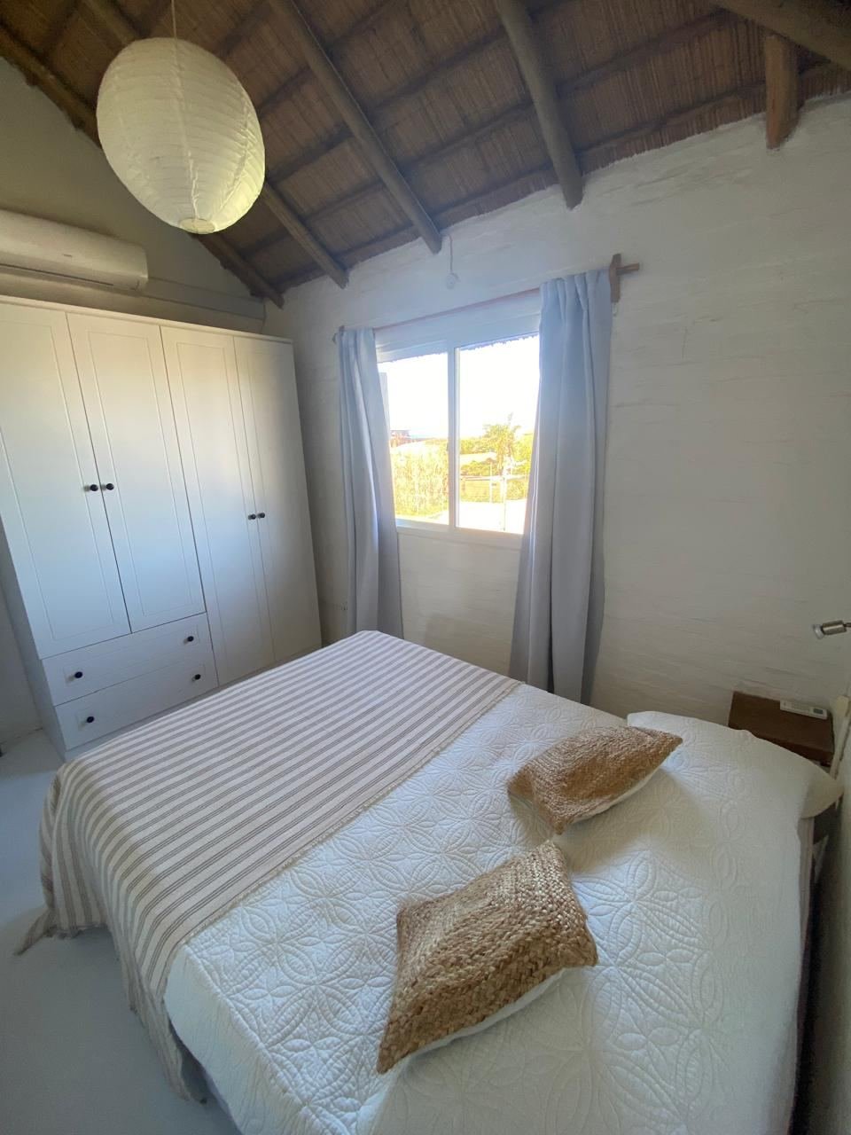 Dormitorio con cama matrimonial, manta a rayas, placard y ventana