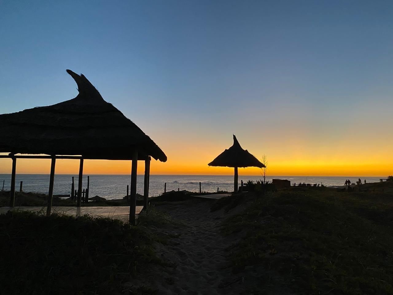 Siluetas de glorietas de paja contra un atardecer naranja sobre el mar