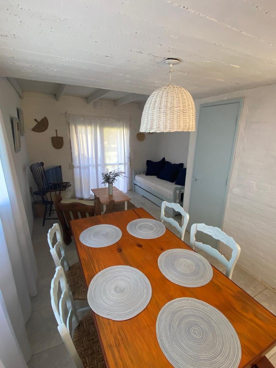 Mesa de madera con individuales tejidos y sillas blancas