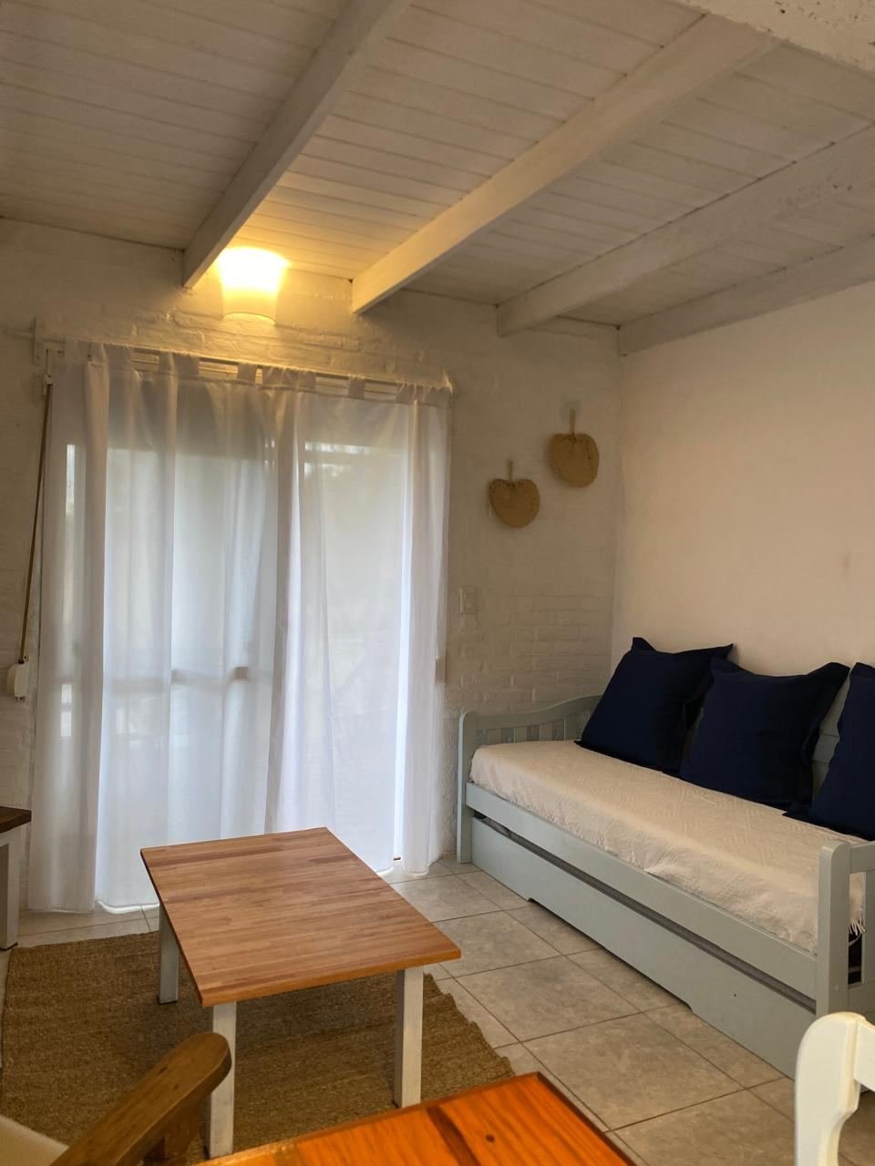 Living con diván cama, almohadones azules y cortinas blancas
